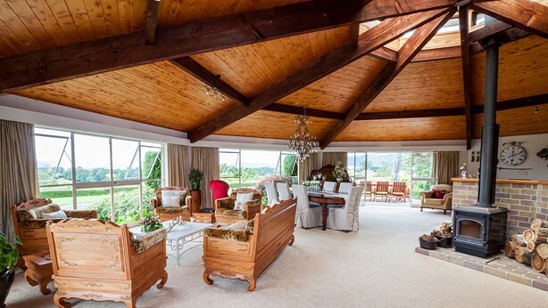 A spacious living room with wooden furniture, a fireplace, and large windows offering a view of the outdoors.