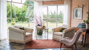 A cozy room with two armchairs, a coffee table, and a view of a garden through large windows.