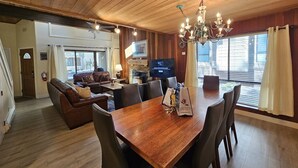 A spacious living room with a wooden ceiling, a dining area with a wooden table and chairs, a fireplace, and a television.