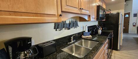 A kitchen with wooden cabinets, a stainless steel sink, a black countertop, and a black refrigerator.