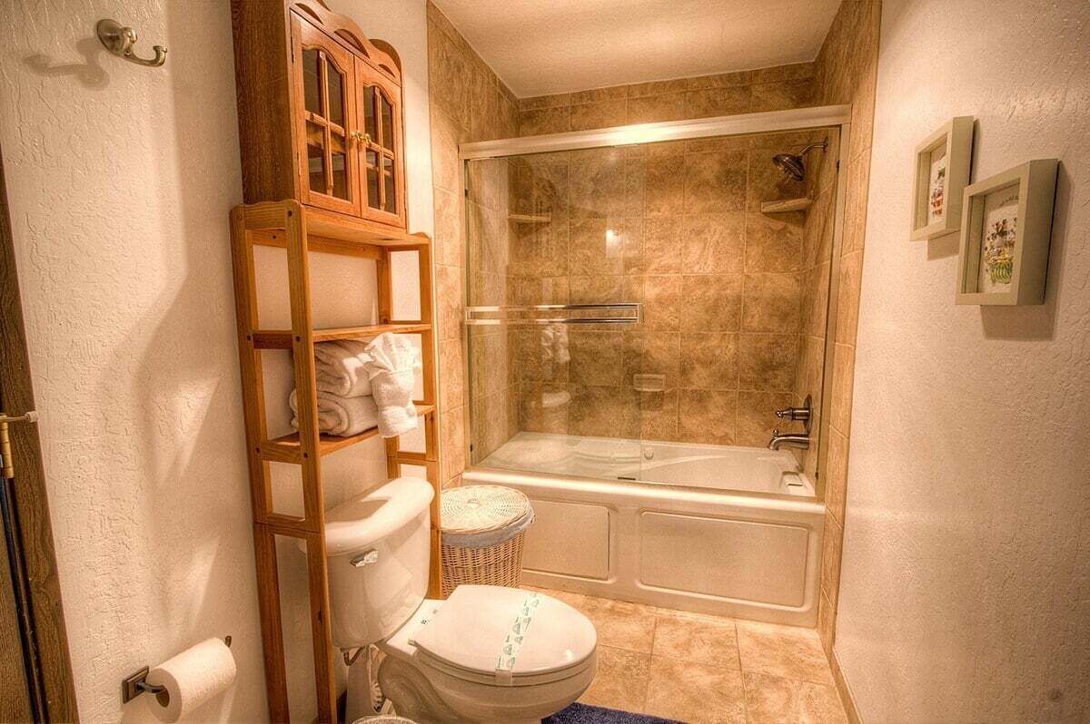 A bathroom with a toilet, a wooden shelf with towels, a glass-enclosed shower, and a bathtub.