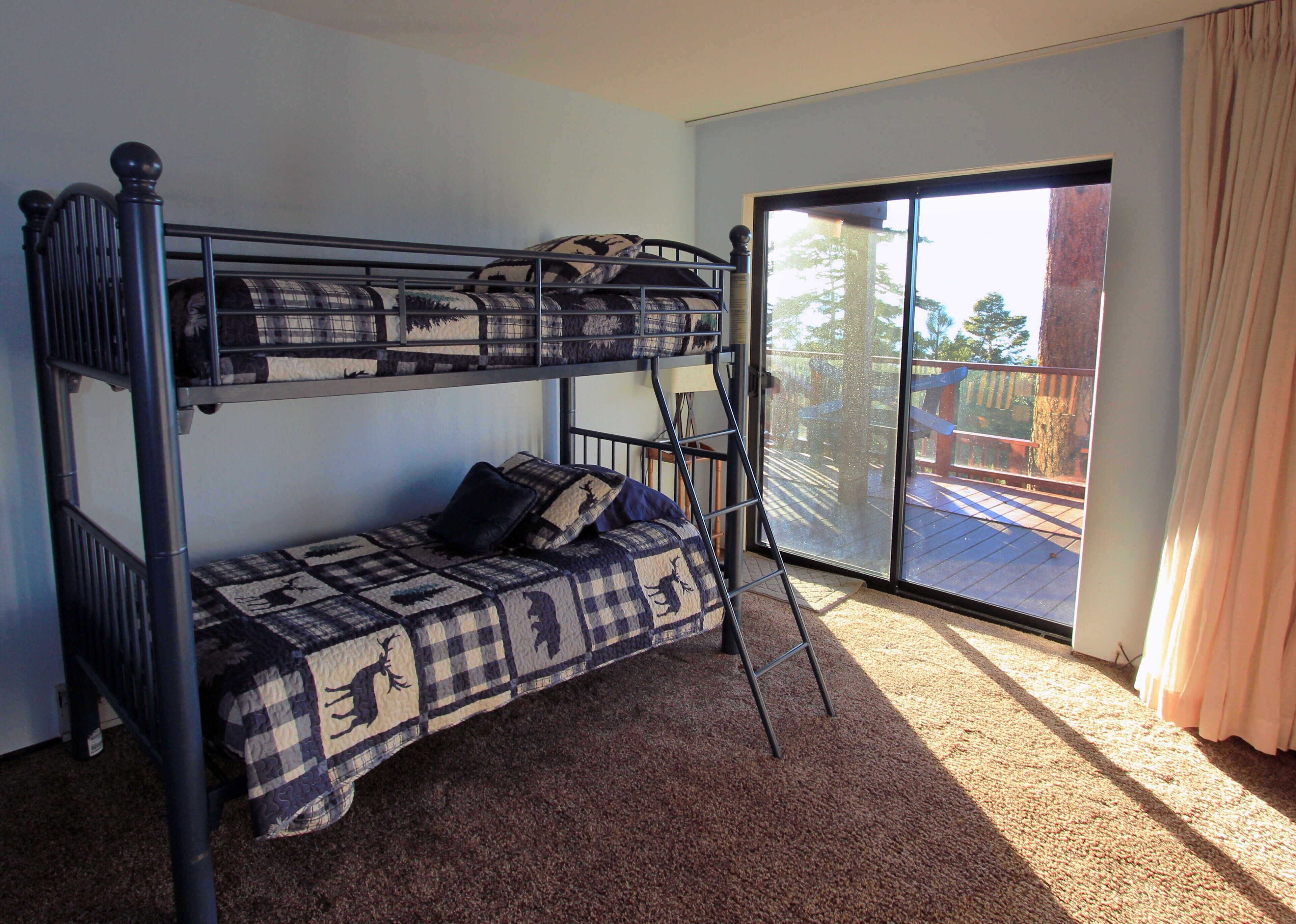 A bunk bed room with a checkered bedspread, a ladder, and a view of a deck through a glass door.