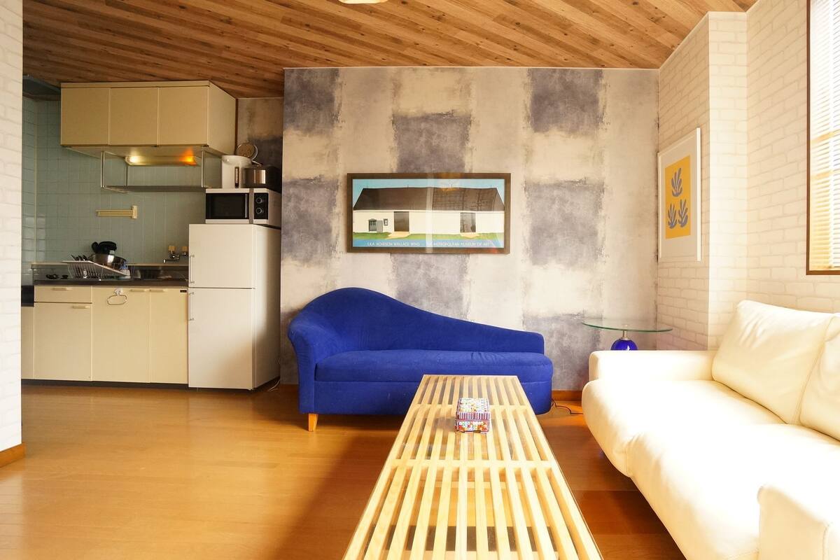 A compact living space with a kitchenette, a blue sofa, a white sofa, and a wooden coffee table.