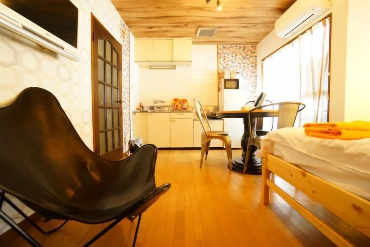 Una habitación pequeña con cama, una silla, una mesa y kitchenette.