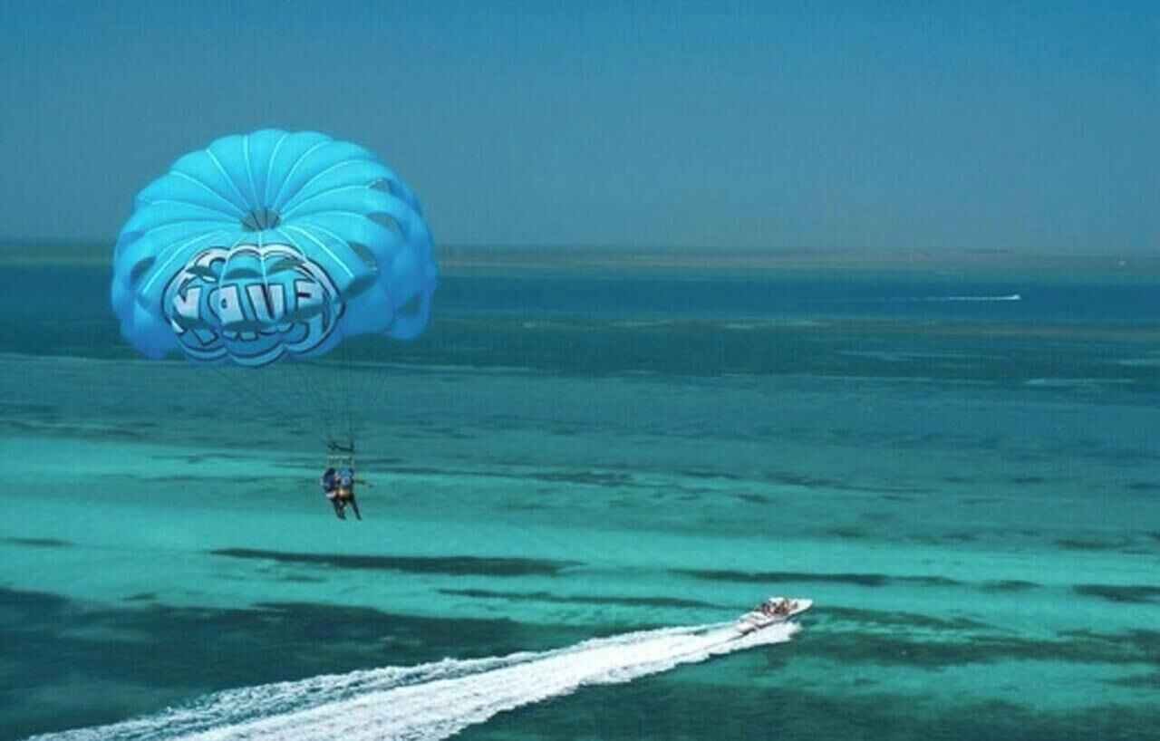 A parasailer over turquoise water with a wakeboarder.