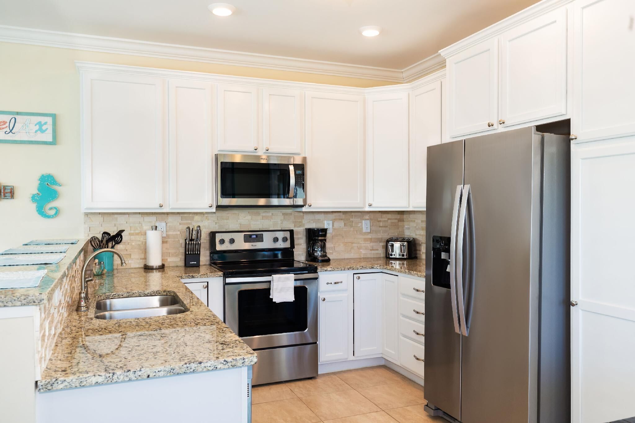 A modern kitchen with white cabinets, stainless steel appliances, granite countertops, and a tiled backsplash.