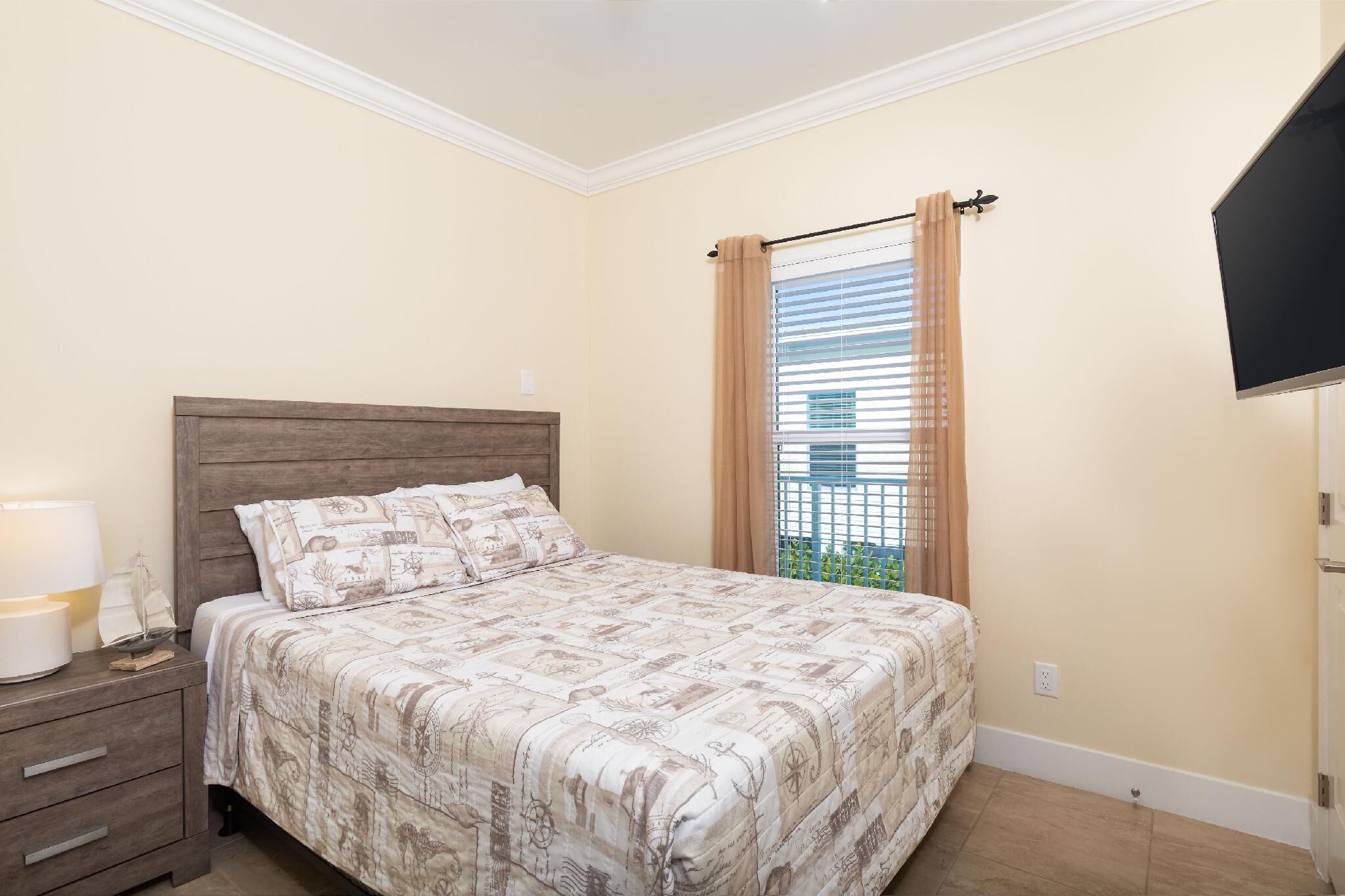 Une chambre à coucher avec une tête de lit en bois, un lit recouvert d’une literie à motifs, une table de chevet avec une lampe et une fenêtre avec des rideaux.