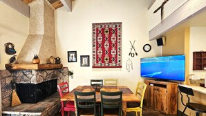 A cozy living room with a stone fireplace, a TV, and a dining area with wooden furniture.
