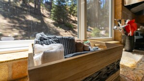 A wooden bench with towels and a tray, a window with a forest view, and kitchen utensils in the background. - Walk to Beach | Pet-Friendly | Deck | BBQ (Zephyr Cove)