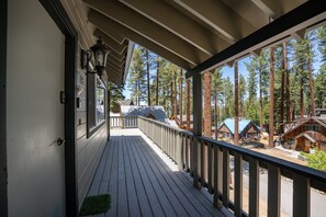 Eine Holzterrasse mit Geländer, die auf einen bewaldeten Bereich mit Blockhütten blickt.