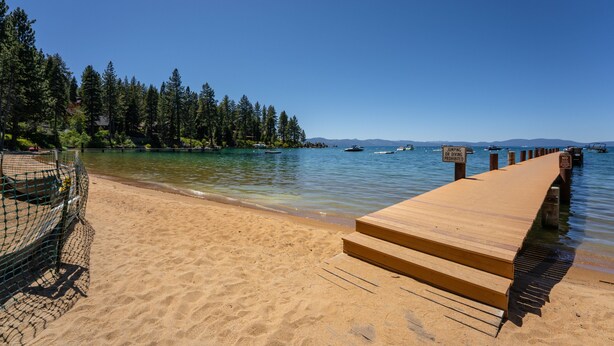A beach with a wooden pier, clear blue water, and a forested area in the background. - Walk to Beach | Pet-Friendly | Deck | BBQ (Zephyr Cove)