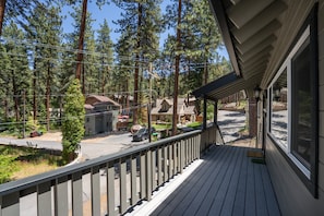 A wooden deck with a railing overlooking a residential street with houses and a clear sky.