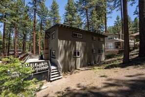 A two-story cabin with a deck, surrounded by tall pine trees. - Walk to Beach | Pet-Friendly | Deck | BBQ (Zephyr Cove)