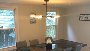 Ein Essbereich mit Holztisch, sechs Stühlen, einer Vase und einer Pendelleuchte.
