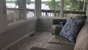 Ein gemütliches Zimmer mit einem beigen Sofa, einem Teleskop und großen Fenstern mit Blick auf einen See.