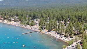 An aerial view of a coastal area with a beach, dense forest, and a pier. - Beachside Bungalo | Deck | BBQ (Kings Beach)