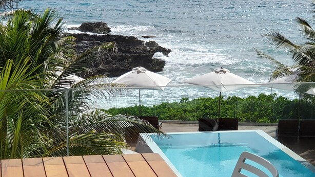 A poolside area with a view of the ocean, a wooden table, and a white chair. - Hotel Secreto (Isla Mujeres)
