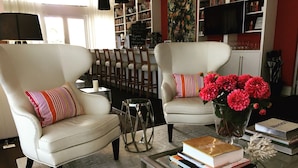 A living room with two white armchairs, a glass coffee table with books, a vase with flowers, and a bookshelf in the background. - Hotel Secreto (Isla Mujeres)