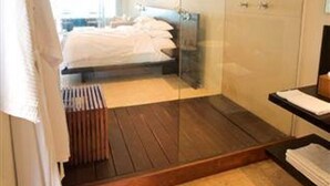 A modern bedroom with a glass shower enclosure, a wooden floor, and a bed with white linens. - Hotel Secreto (Isla Mujeres)