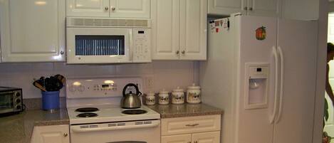 A kitchen with white cabinets, a microwave, a stove, and a refrigerator.
