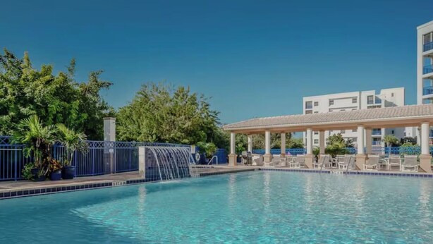 A swimming pool with a waterfall feature, surrounded by lounge chairs and a covered seating area. - Sunny 3BR/ 2bath w/ Hot Tub~Beach Access + Pool + Tennis + BBQ + Gated Community (New Smyrna Beach)