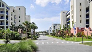 A street view with modern multi-story buildings, a pedestrian crossing, and a stop sign. - Sunny 3BR/ 2bath w/ Hot Tub~Beach Access + Pool + Tennis + BBQ + Gated Community (New Smyrna Beach)