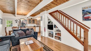 Un vaste espace de vie doté d’un plafond en bois, d’un escalier et d’une cuisine en arrière-plan.