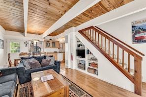 Un vaste espace de vie dotĂ© dâun plafond en bois, dâun escalier et dâune cuisine en arriĂšre-plan.