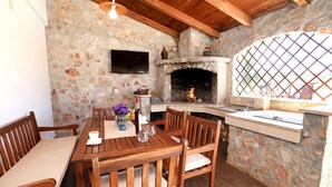 Cocina de paredes de piedra con chimenea, mesa de madera y sillas.