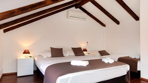 Un dormitorio con dos camas, vigas de madera en el techo, una mesita de noche blanca con lámpara y aire acondicionado de pared.