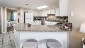 A modern kitchen with white cabinets, granite countertops, and two bar stools. - Nautilus 2310  Gulf View 2BD/2BA 3rd Floor.  Free Beach Service 3/1-10/31 (Ft Walton Beach)