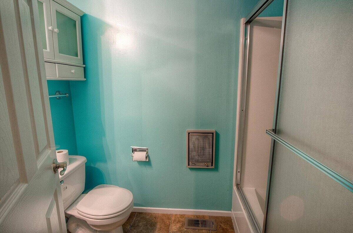 A bathroom with a toilet, a cabinet, a towel dispenser, and a ventilation unit.
