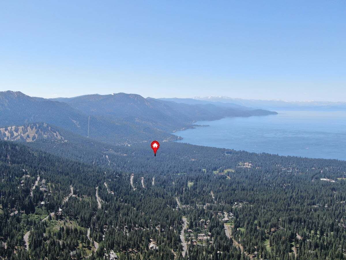 Paisaje montañoso con una masa de agua, un marcador rojo que indica una ubicación y un bosque denso.