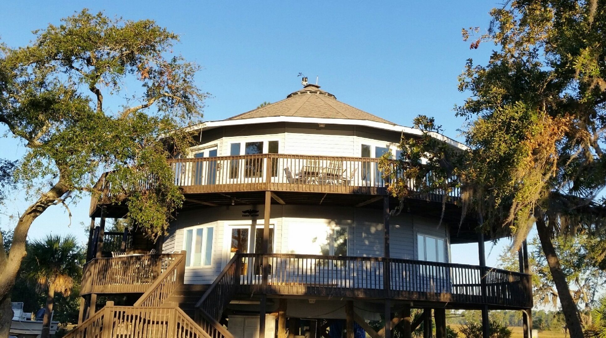 A two-story wooden structure with a balcony, surrounded by trees.