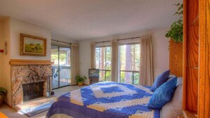 Ein Schlafzimmer mit einem großen Bett, Kamin, Fernseher und einem Balkon mit Vorhängen.