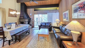 A living room with a wooden ceiling, a stone fireplace, a dining table, leather sofas, and a lamp. - Kingswood Condo | Community Pool (Kings Beach)