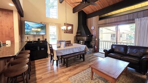 A spacious living area with a wooden ceiling, a stone fireplace, a dining table, and a leather couch. - Kingswood Condo | Community Pool (Kings Beach)