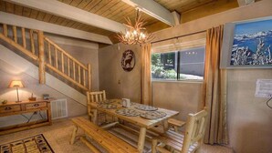 Un tavolo da pranzo in legno con panche, un lampadario, una scala e una finestra che offre vista sulle montagne.