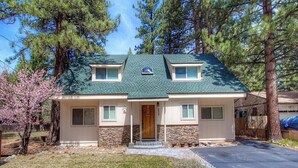 A two-story house with a green roof, stone foundation, and a front porch.