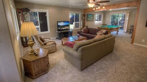 A living room with a sofa, armchair, coffee table, TV, and pool table.