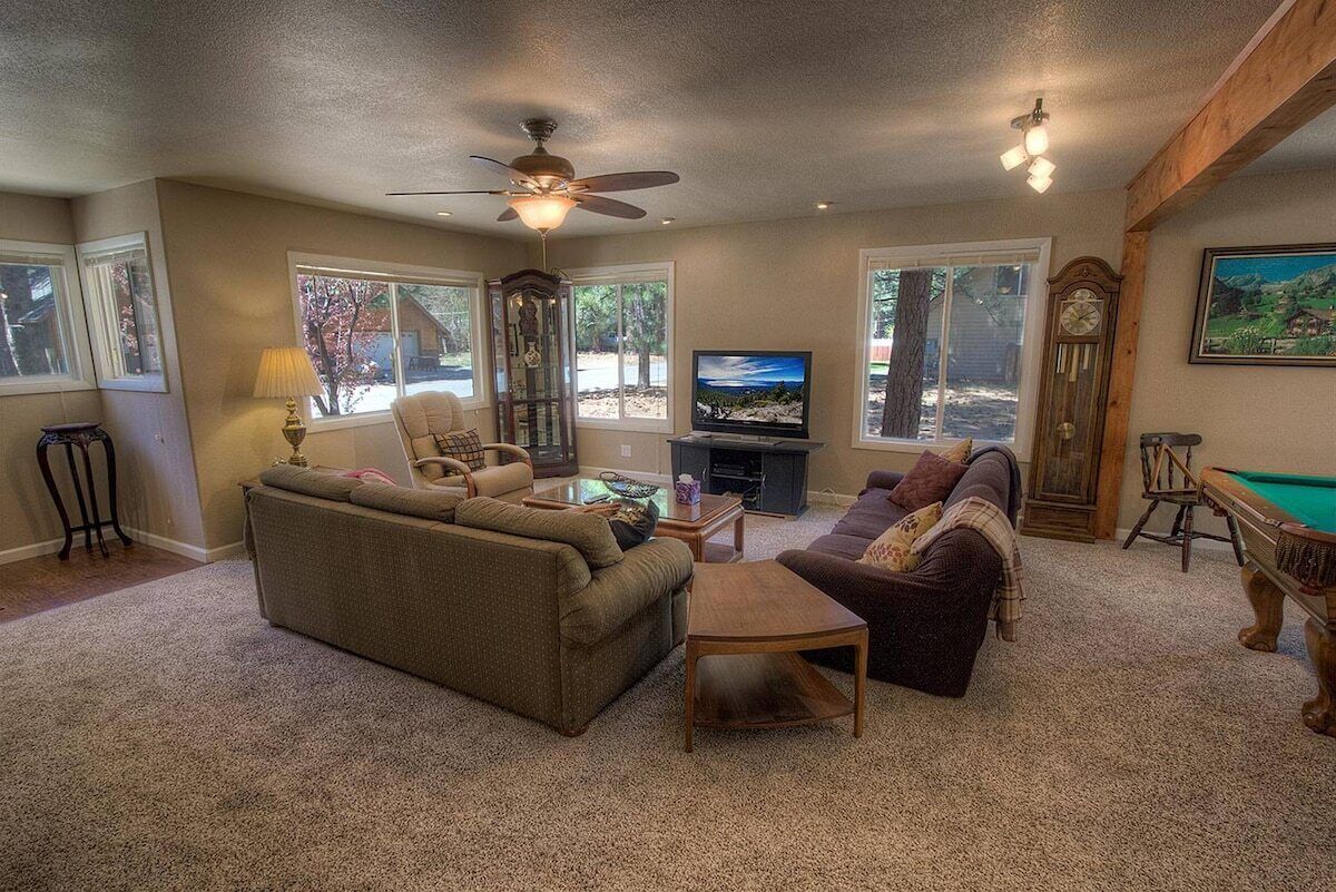 Een woonkamer met een bank, fauteuil, salontafel, televisie en een pooltafel.