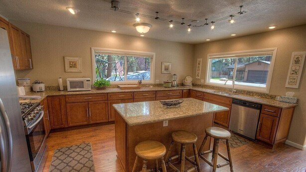 A modern kitchen with wooden cabinets, a granite island, bar stools, and a dishwasher.