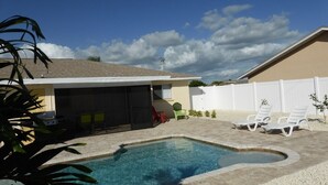 Un patio trasero con piscina, zona de barbacoa y mobiliario exterior.