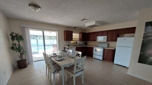 Una cocina moderna con armarios de madera oscura, electrodomésticos blancos y un comedor con una mesa lista para cuatro comensales.