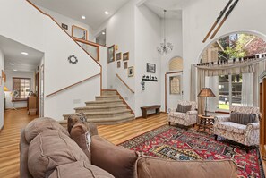 A spacious living room with a staircase, a large window, and a patterned rug.