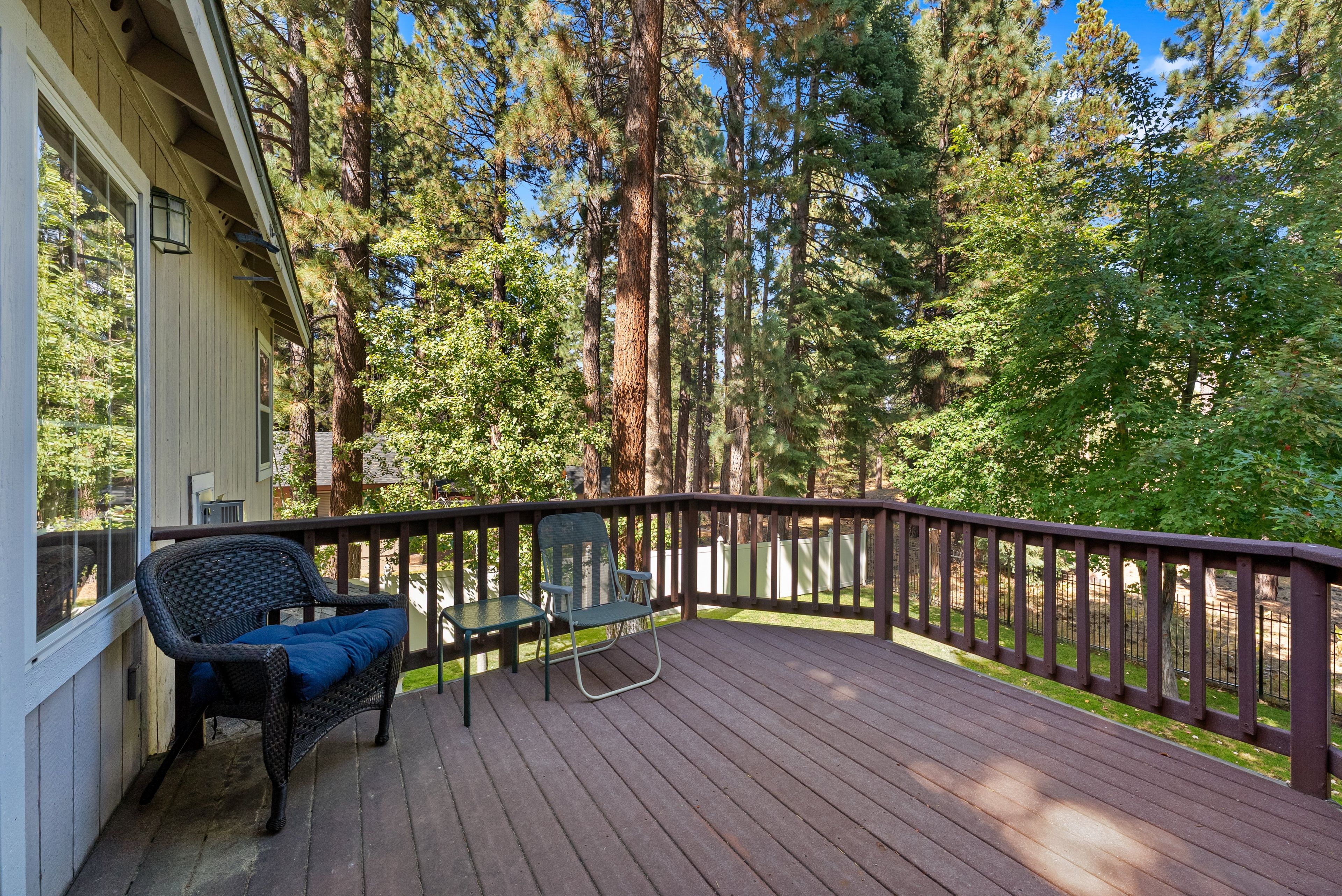 A wooden deck with a railing, two chairs, and a table.