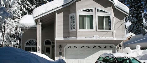 A two-story house with a garage, surrounded by snow-covered trees.