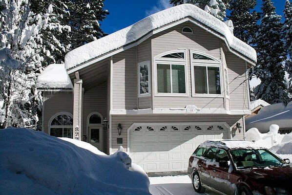 Una casa de dos pisos con garaje, rodeada de árboles cubiertos de nieve.