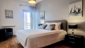 A bedroom with a bed, a nightstand, a lamp, a window with curtains, and sailboat artwork on the walls.