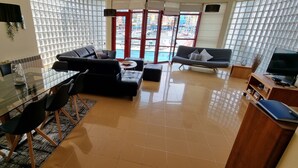 A modern living room with a glass dining table, black sofas, and a TV.